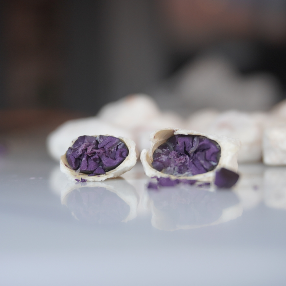 Two halves of a white shell with purple interior on a reflective surface.