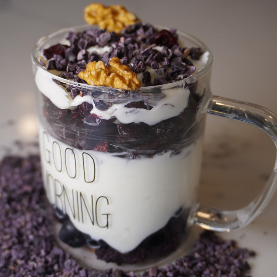 Glass mug with layered dessert, nuts, and 'Good Morning' text on a blurred background
