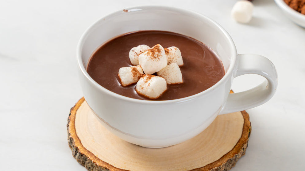 Hot chocolate with marshmallows in a white mug on a wooden coaster.