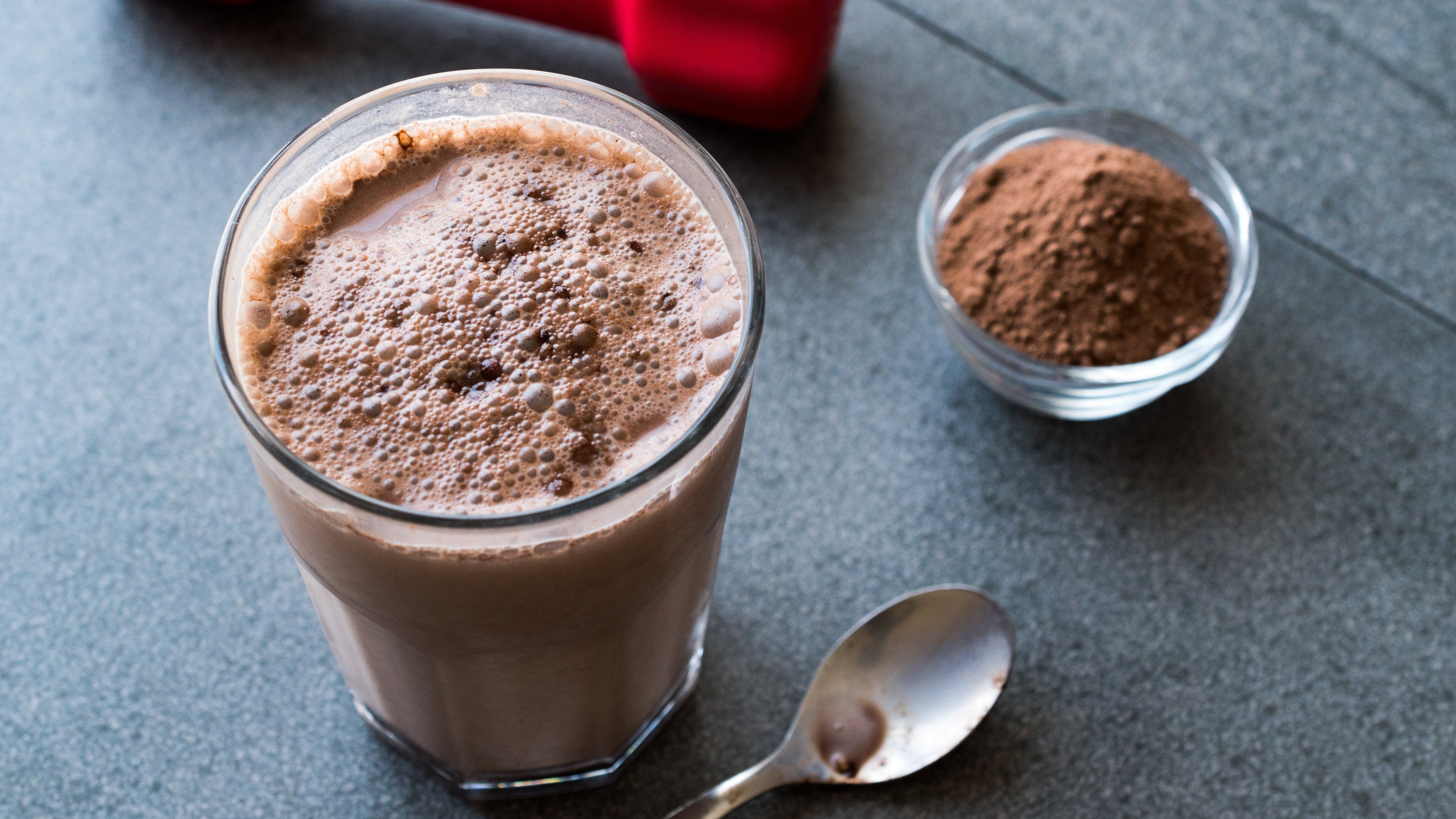 Chocolate protein shake in a glass with cocoa powder and a spoon on a gray surface