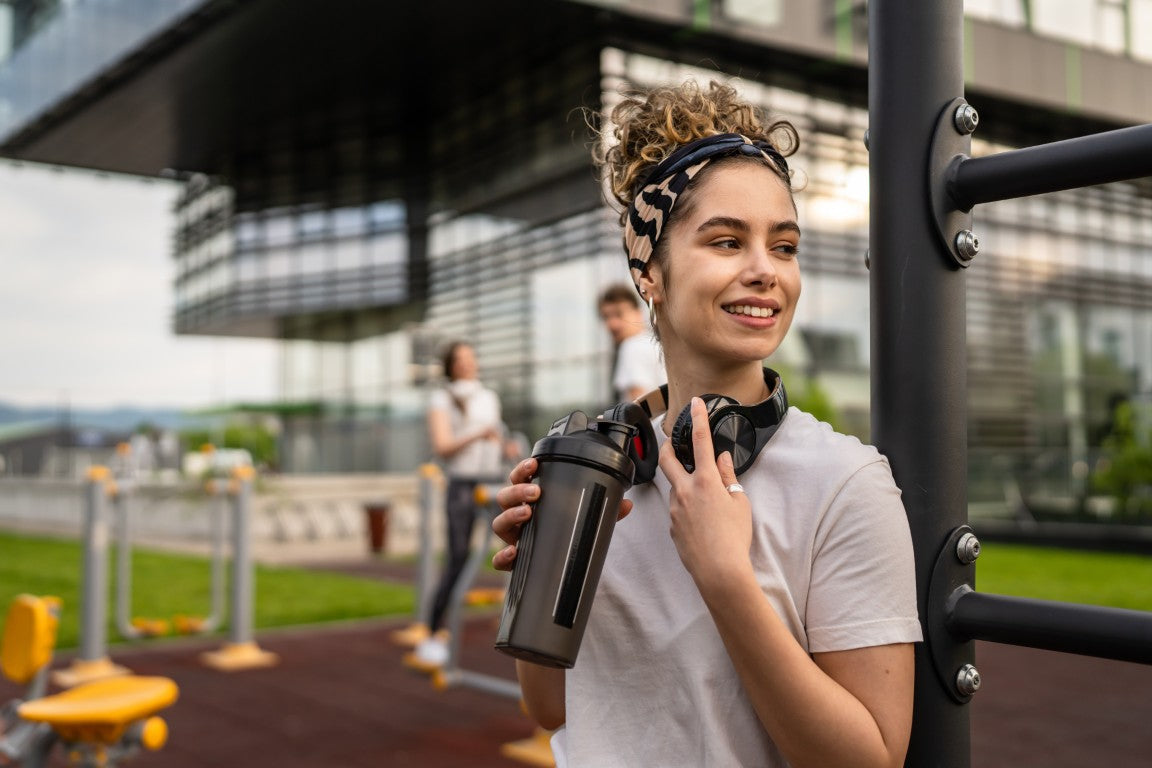 Woman holding a water bottle and headphones in an outdoor fitness area