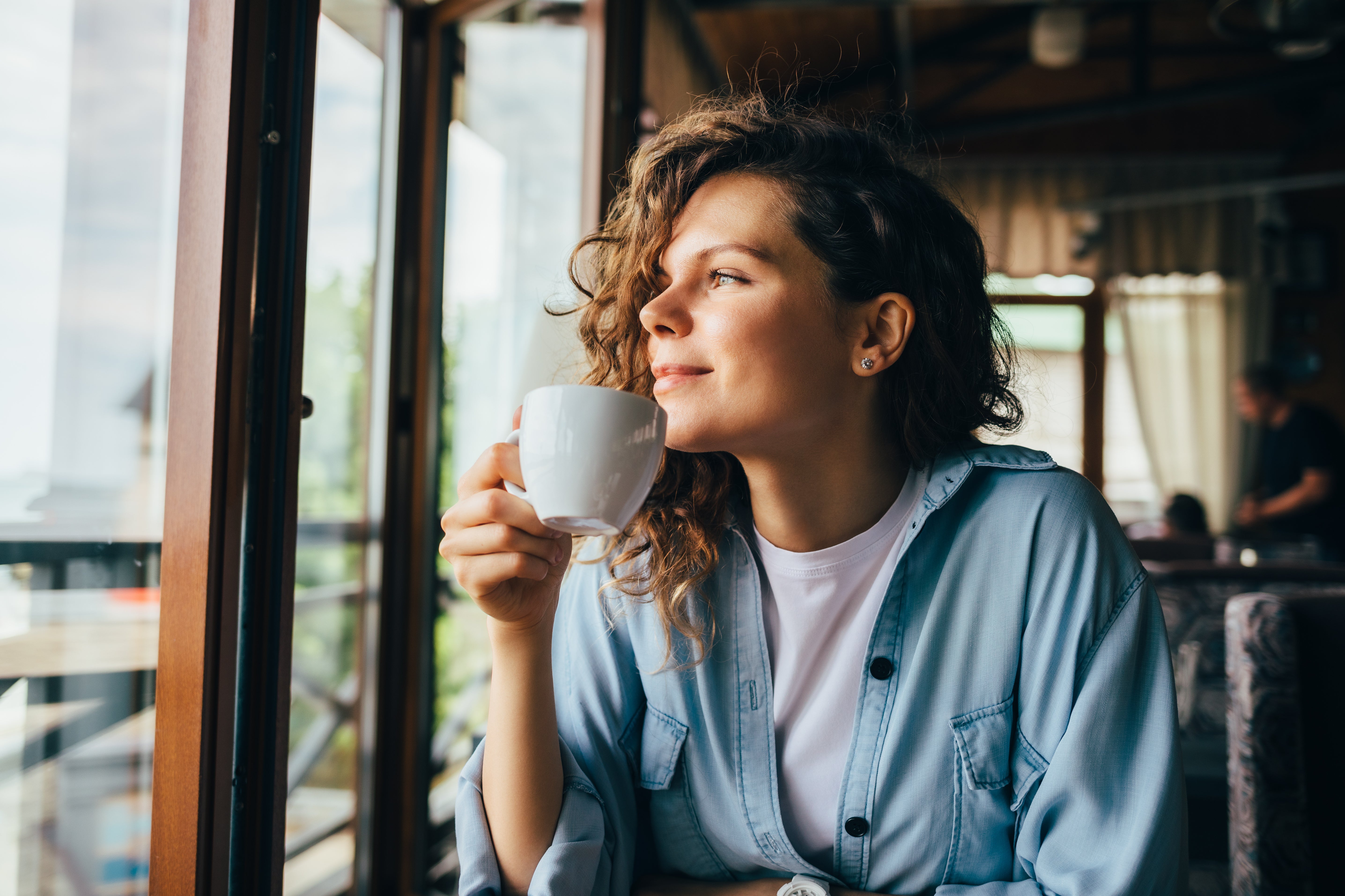 Woman holding a white mug, sitting by a window in a casual setting
