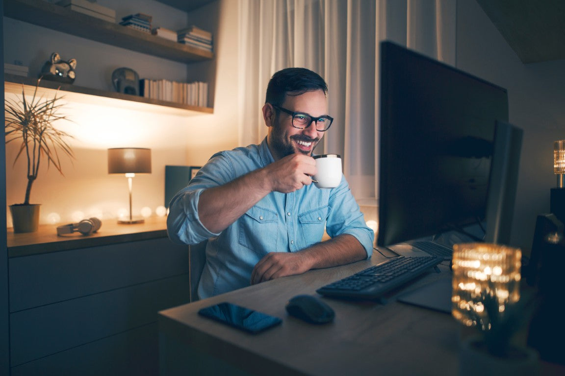 Man sitting at a desk in a home office, holding a mug and smiling.