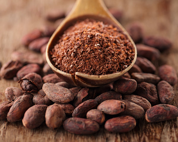 Cocoa beans with a wooden spoon filled with ground cocoa powder on a wooden surface